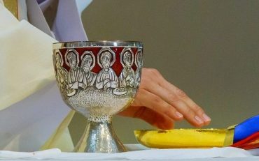 Holy communion on table in church cup of glass with red wine, and Holy Bible
